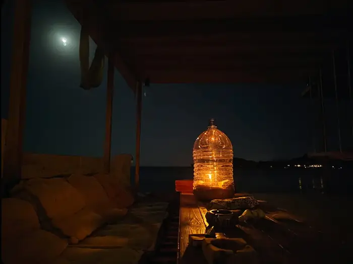 A glowing glass jug on the deck railing beneath the moon at night