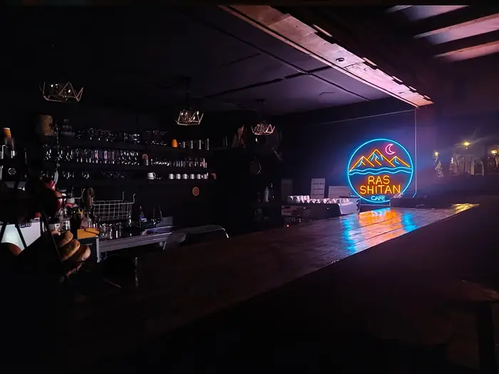 The neon Ras Shitan Cafe sign glowing above the bar counter at night