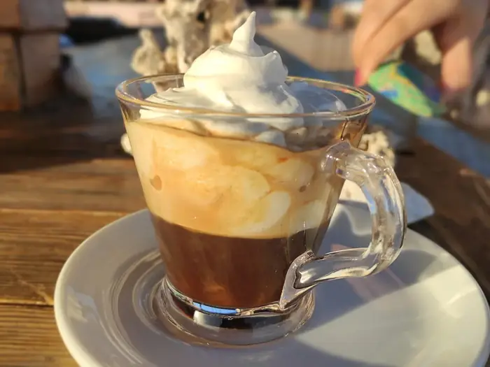 A layered coffee topped with whipped cream in a glass mug on a wooden table