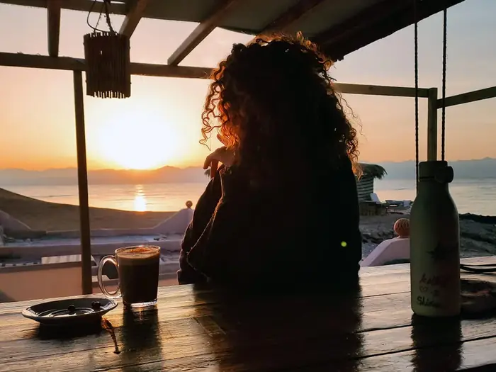 Silhouette of a guest at a wooden table watching the sun set over the water