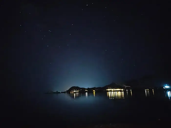 A starlit night over the Red Sea, with distant shoreline lights reflecting on the calm water