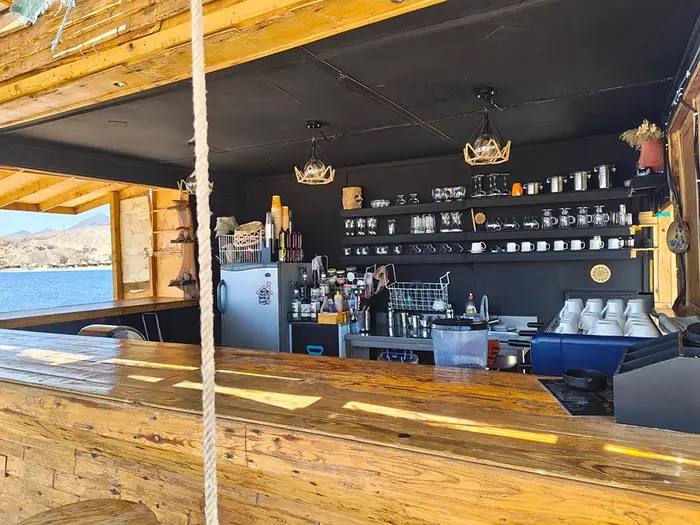 The rustic wooden bar counter and shelves, with the sea framed by the open window
