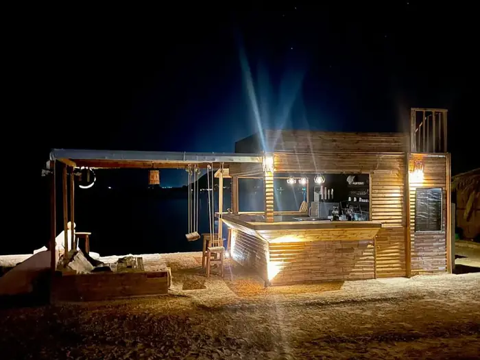 The beach bar lit up at night, with beams of light shining into the dark sky